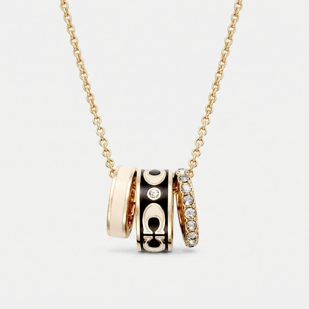 A gold chain necklace with a multi-band pendant featuring gold, black enamel, and diamond accents, shown on a light gray background.