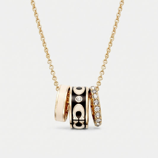 A gold chain necklace with a multi-band pendant featuring gold, black enamel, and diamond accents, shown on a light gray background.