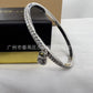 A silver-toned bangle bracelet with a row of clear stones and a small padlock charm, displayed on a white surface with a black jewelry box in the background.