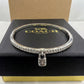 A silver-tone Coach bangle bracelet with a padlock charm, displayed on its black textured brand box.
