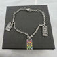 A silver-tone chain bracelet with three rectangular charms, one of which is decorated with a colorful floral pattern in pink, orange, yellow, green, and blue. The bracelet is displayed on a textured black presentation box.