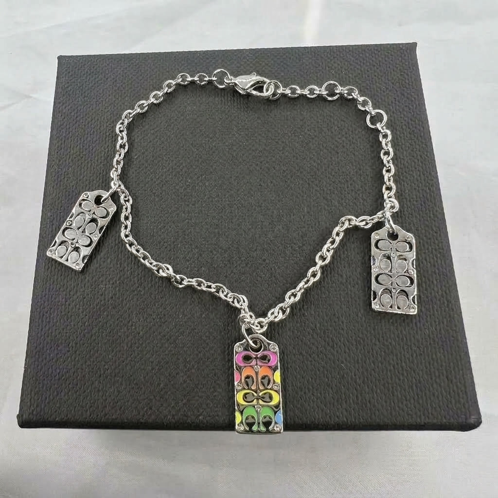 A silver-tone chain bracelet with three rectangular charms, one of which is decorated with a colorful floral pattern in pink, orange, yellow, green, and blue. The bracelet is displayed on a textured black presentation box.