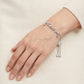 A delicate silver bracelet with the name 'Coach' in cursive script and dangling charm elements, shown worn on a person's wrist against a soft cream-colored knit background.