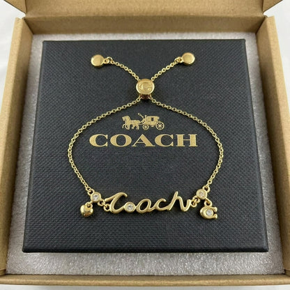 A gold-tone Coach nameplate bracelet with crystal accents, presented on its black branded box inside an open brown presentation box.