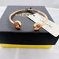 A Coach cuff bracelet in rose gold with two round crystal-encrusted end caps, displayed on top of a black Coach box with a white brand tag.