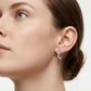 A close-up of a woman's ear wearing a small silver hoop earring set with clear stones, against a clean white background.