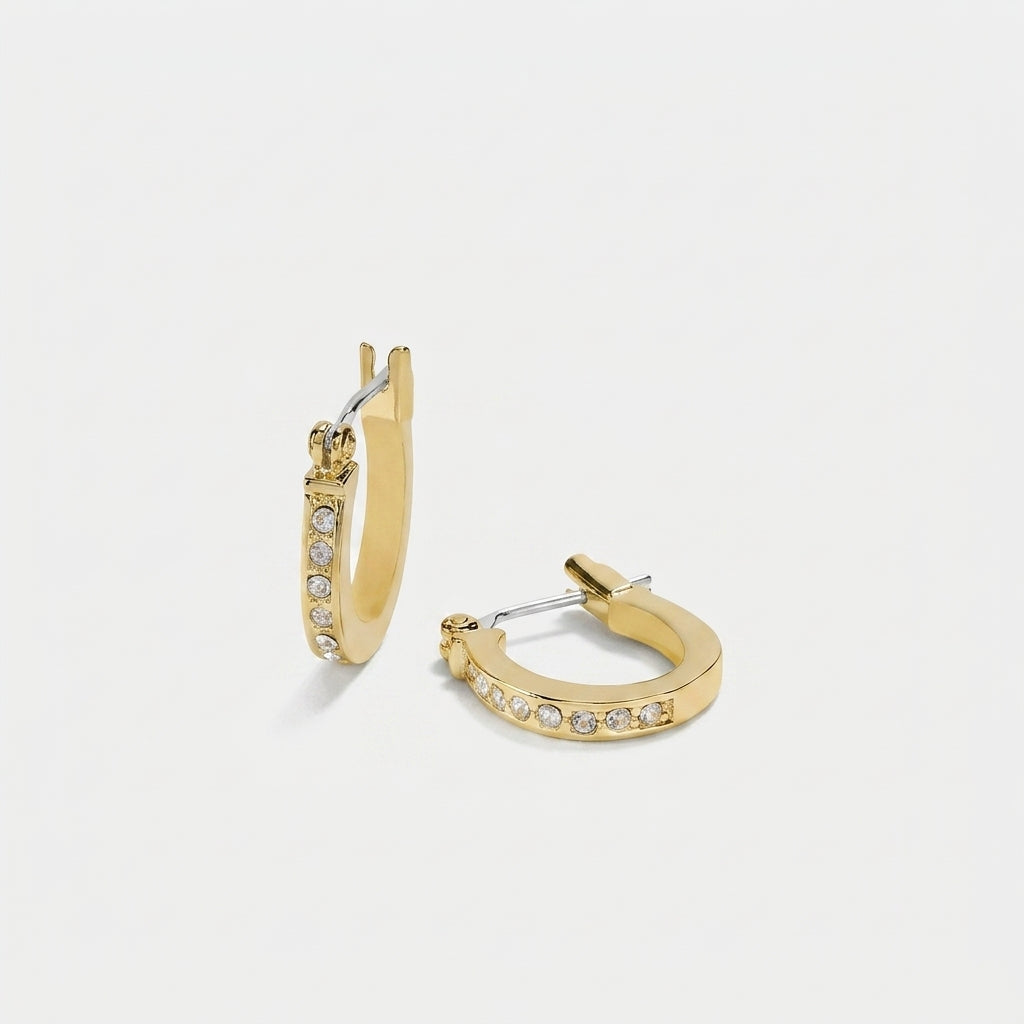 A pair of gold huggie hoop earrings with a row of small clear pavé stones along the front, displayed on a clean light gray background.