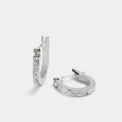 A pair of silver huggie hoop earrings with clear pavé-set stones, shown from two angles on a light gray background.