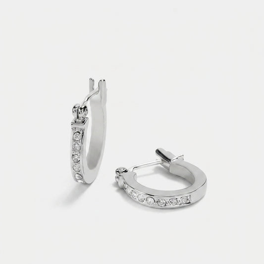 A pair of silver huggie hoop earrings with clear pavé-set stones, shown from two angles on a light gray background.