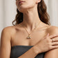 A close-up lifestyle shot of a woman wearing a delicate gold necklace with a cherry blossom pendant and a small star charm, paired with a gold ring on her finger.