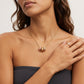 A close-up of a woman wearing a delicate gold chain necklace with a small cylindrical pendant featuring pink and gold textured details, paired with a gold ring on her finger.