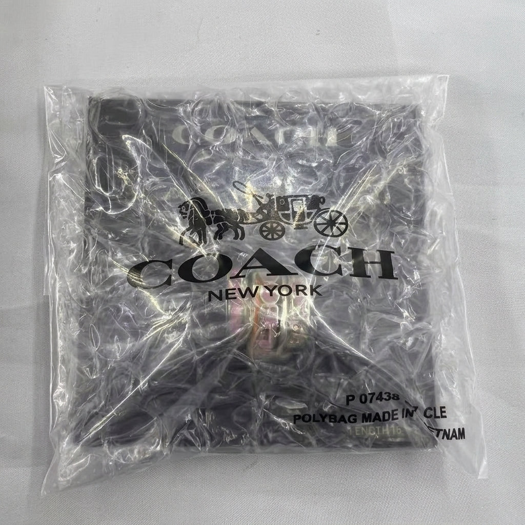 A Coach New York logo printed on a black garment inside a clear plastic protective polybag, photographed against a light gray background.