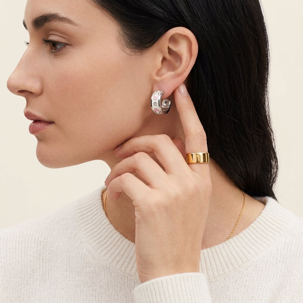 A close-up of a woman wearing a silver crescent-shaped hoop earring with clear crystals and a gold ring, shown in profile against a light cream background.