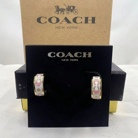 A pair of Coach New York hoop earrings displayed on a black branded card, with the kraft Coach box behind them on a white studio background.