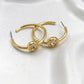 A pair of gold hoop earrings with circular disc charms featuring clear rhinestones and the word 'HOKYO' engraved on the side, displayed on a white textured surface.