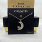 A silver-tone Coach necklace with a crescent moon and star pendant, displayed on a black Coach New York card with a gold Coach box behind it.