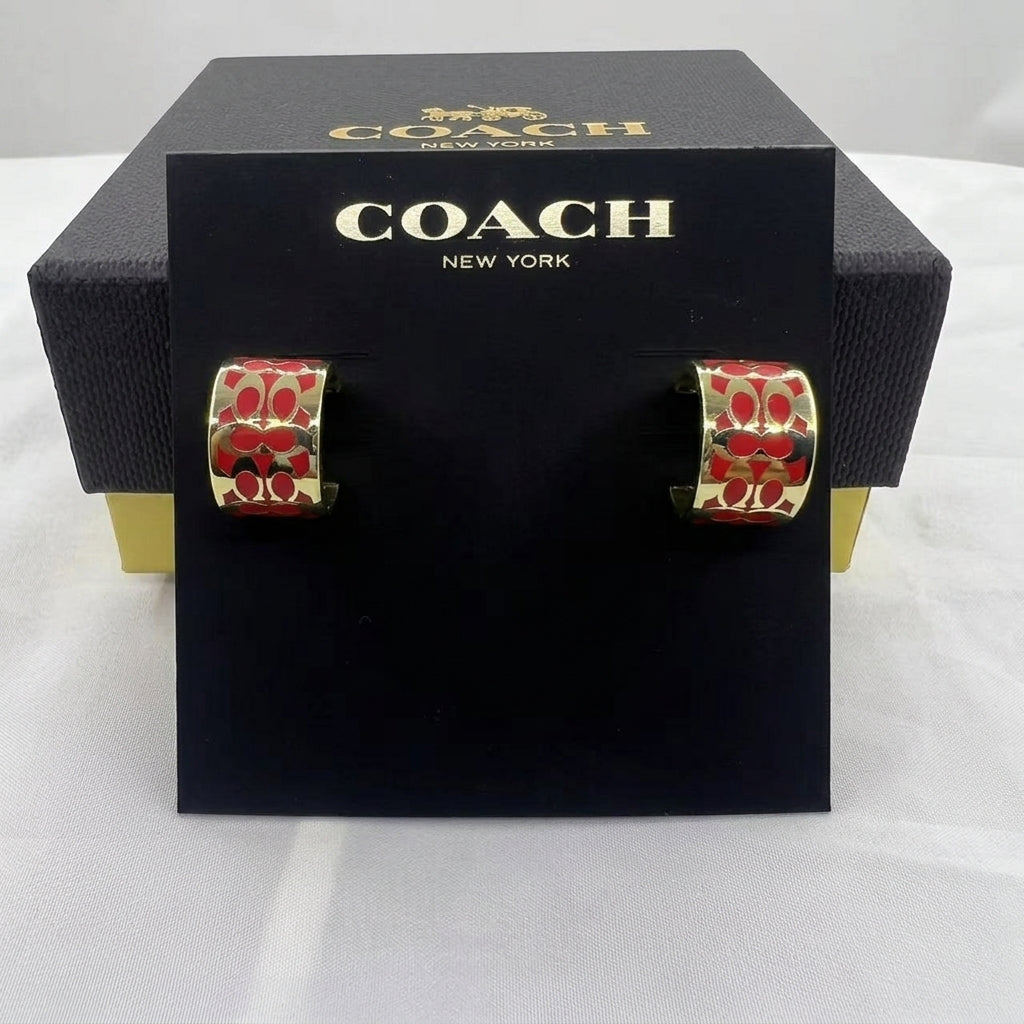 A pair of Coach New York hoop earrings with a red and gold floral pattern, displayed on a black branded card insert in front of a black Coach box.
