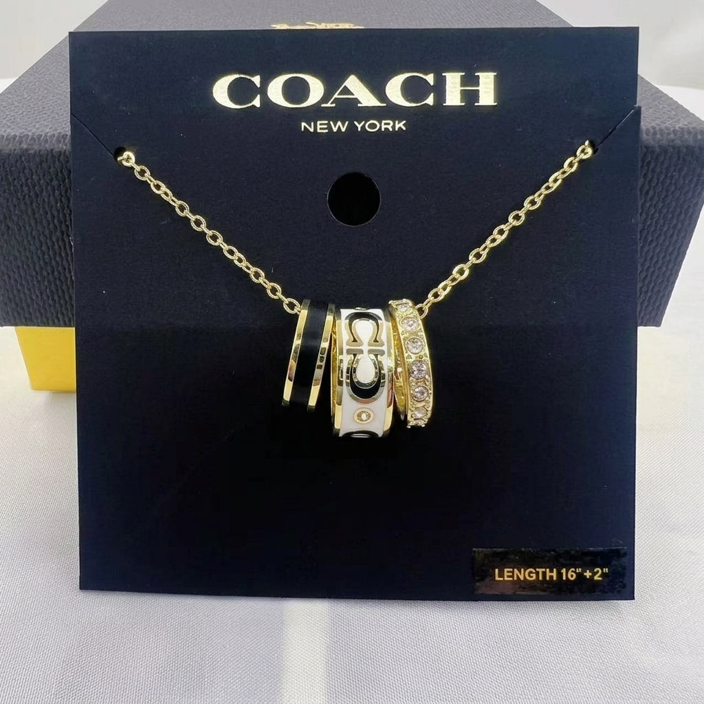 A Coach New York gold chain necklace with a multi-strand charm pendant, displayed on its black branded packaging card.