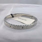 A silver-tone Coach bangle bracelet with engraved 'CO' logos and small crystal accents, shown with a white Coach paper tag on a white fabric background.