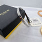 A silver-tone Coach bangle bracelet with engraved logos and small clear stones, displayed next to its black and yellow Coach box and a price tag on a white fabric surface.
