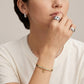A close-up lifestyle shot of a model wearing a delicate gold and silver beaded bracelet on her wrist, along with silver rings and a silver chain necklace.