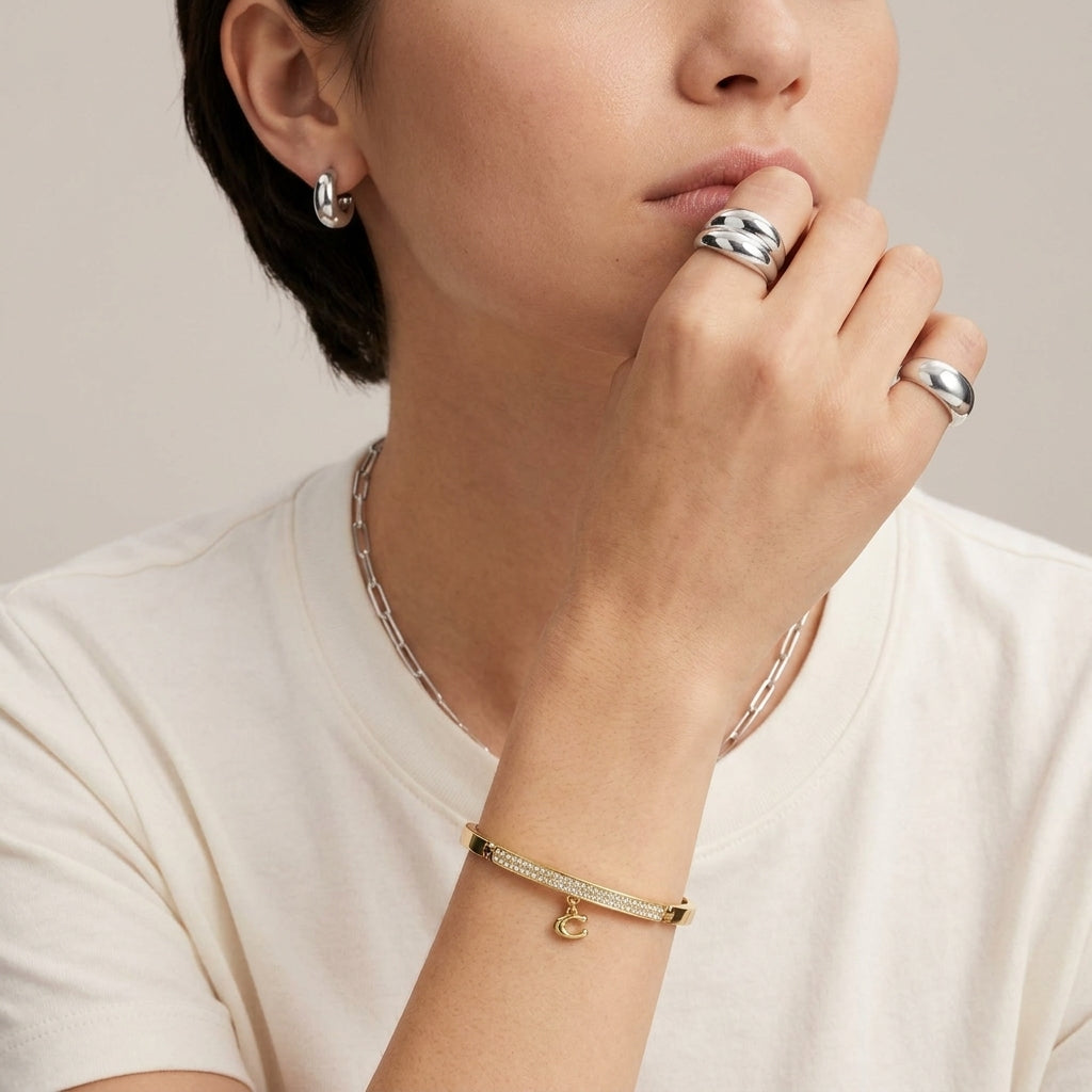 A close-up lifestyle shot of a model wearing a delicate gold and silver beaded bracelet on her wrist, along with silver rings and a silver chain necklace.