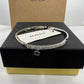 A silver-tone Coach bangle bracelet with a crystal-encrusted band and a small dangling Coach logo charm, displayed on a black Coach presentation box with a gold base.