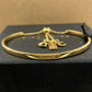 A gold-tone Coach bangle bracelet with a chain extender and three charms (Coach logo, 'COACH' tag, and 'C' charms), resting on a black textured box with the Coach logo visible.