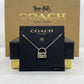A silver padlock necklace on a black display card, with a gold-tone Coach New York box behind it.