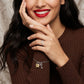 A close-up lifestyle shot of a woman wearing a delicate silver key and lock charm bracelet, a silver wavy ring, and a gold pendant necklace, paired with a brown ribbed sweater.