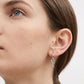 A close-up of a woman's ear wearing a silver key-shaped hoop earring against a clean white background.