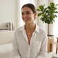  A woman in a soft white blouse and jeans, the layered necklaces resting just above her collarbone.