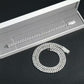 Silver chain bracelet on a textured surface with an open box in the background
