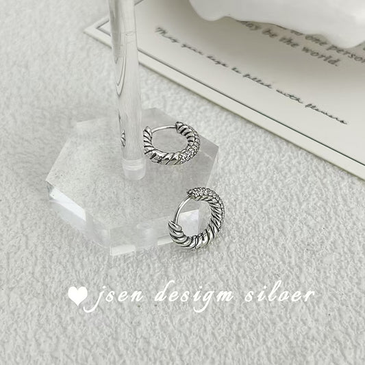 Silver hoop earrings on a clear stand with a soft background