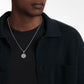 Person wearing a silver necklace with a pendant on a plain background