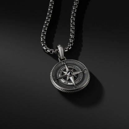 Silver compass pendant on a black chain against a black background