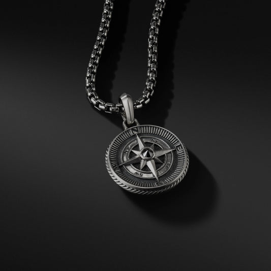 Silver compass pendant on a black chain against a black background