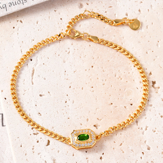 Gold bracelet with a green gemstone on a textured beige surface