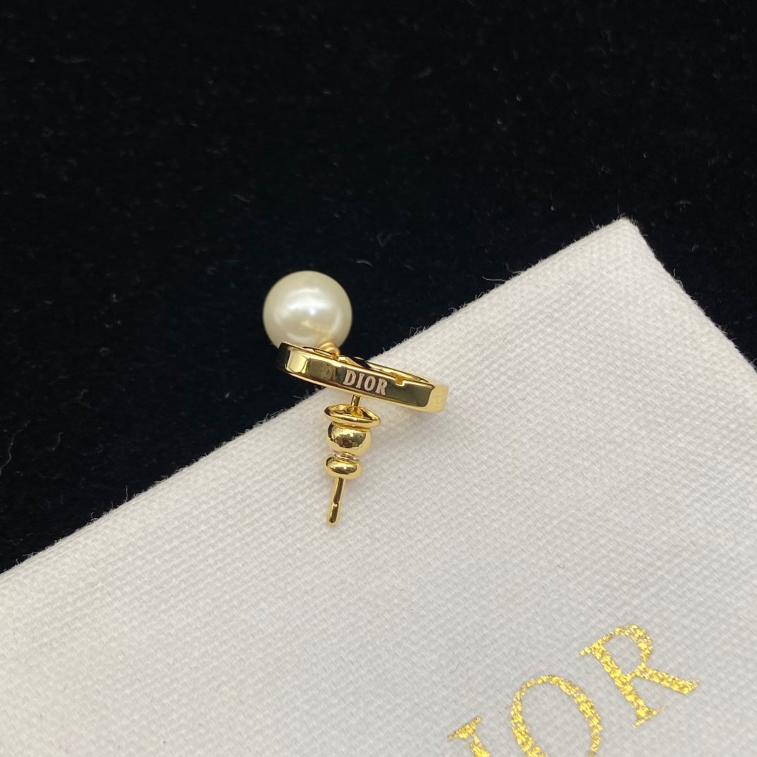 Pearl earring with gold band and 'Dior' logo on a Dior branded cloth background