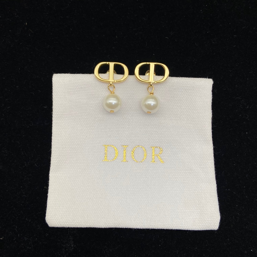 Gold earrings with pearls on a Dior branded pillow against a black background