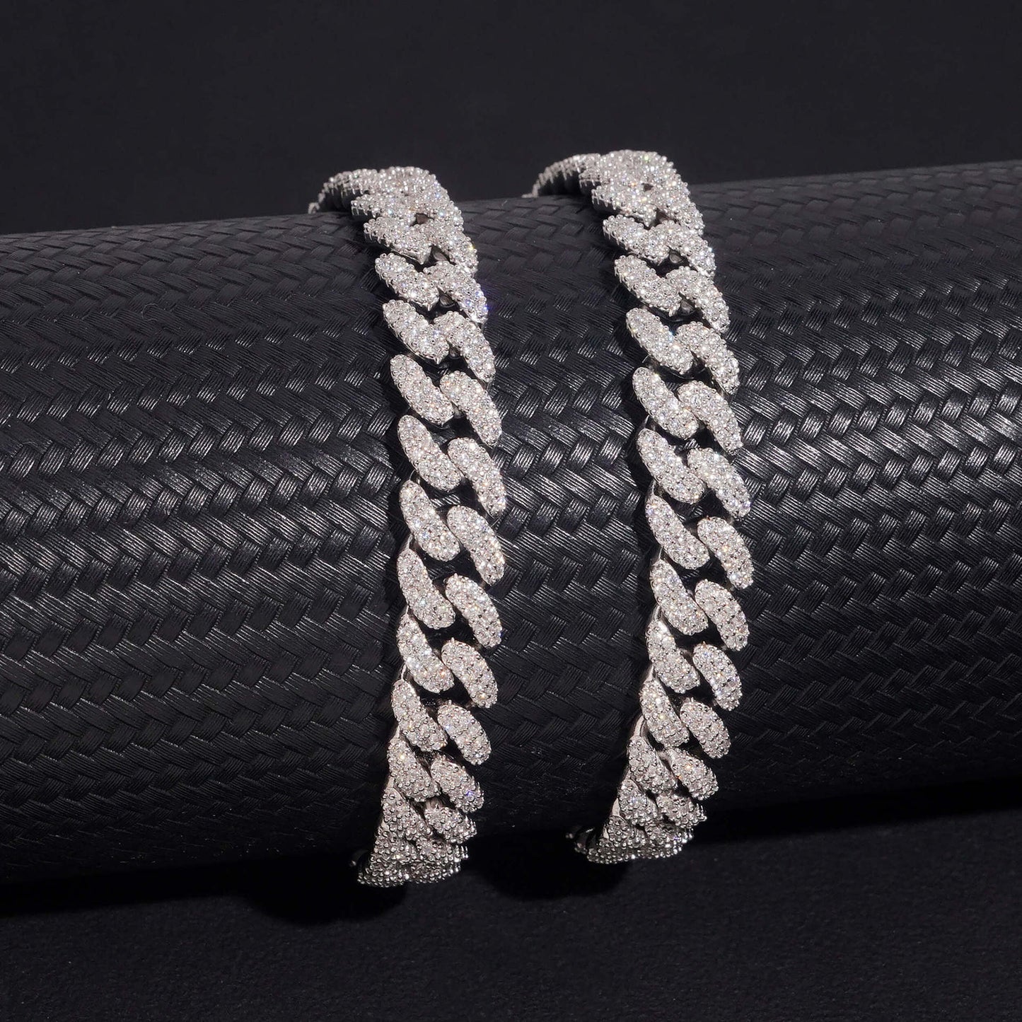 Two diamond-encrusted Cuban links on a black textured surface