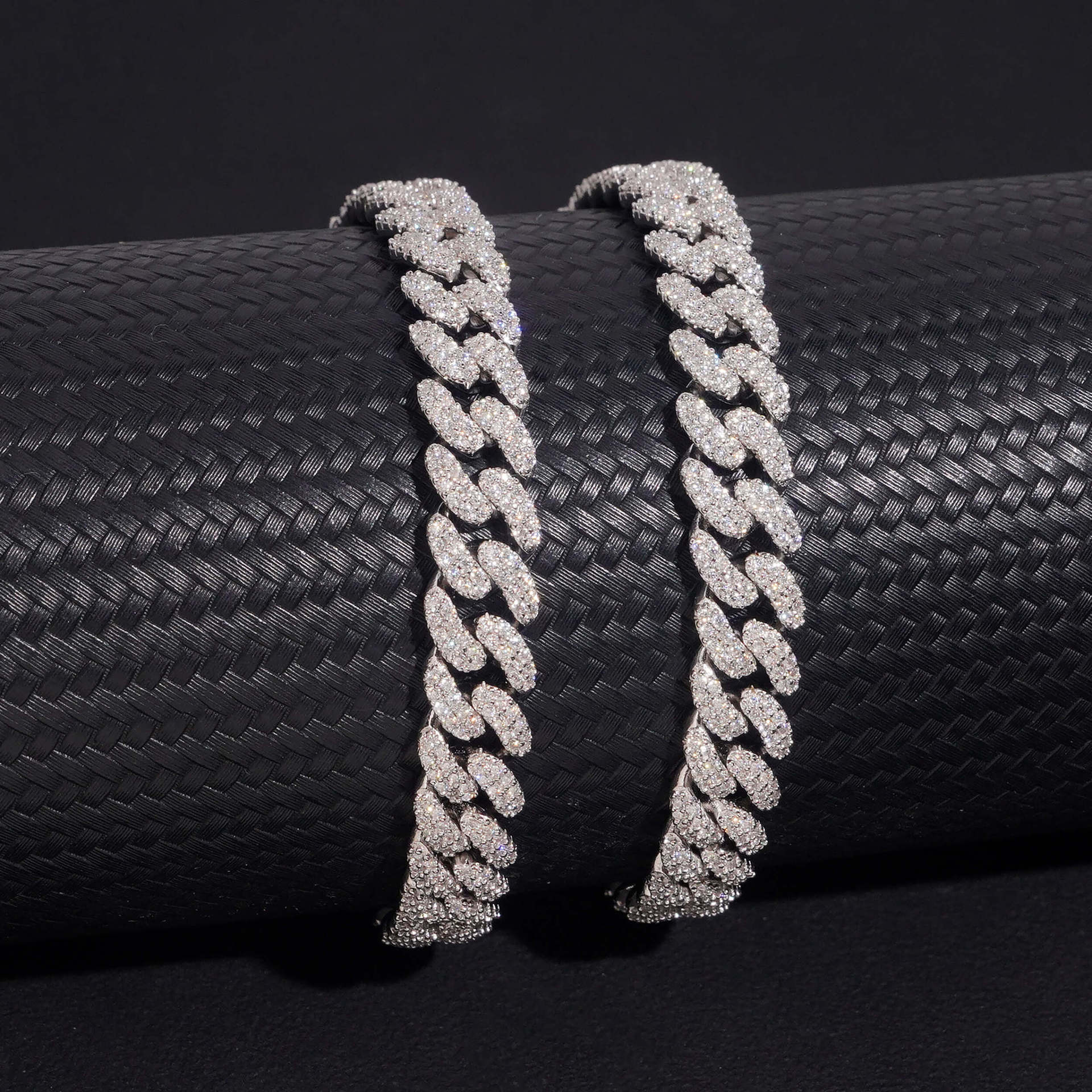 Two diamond-encrusted Cuban links on a black textured surface