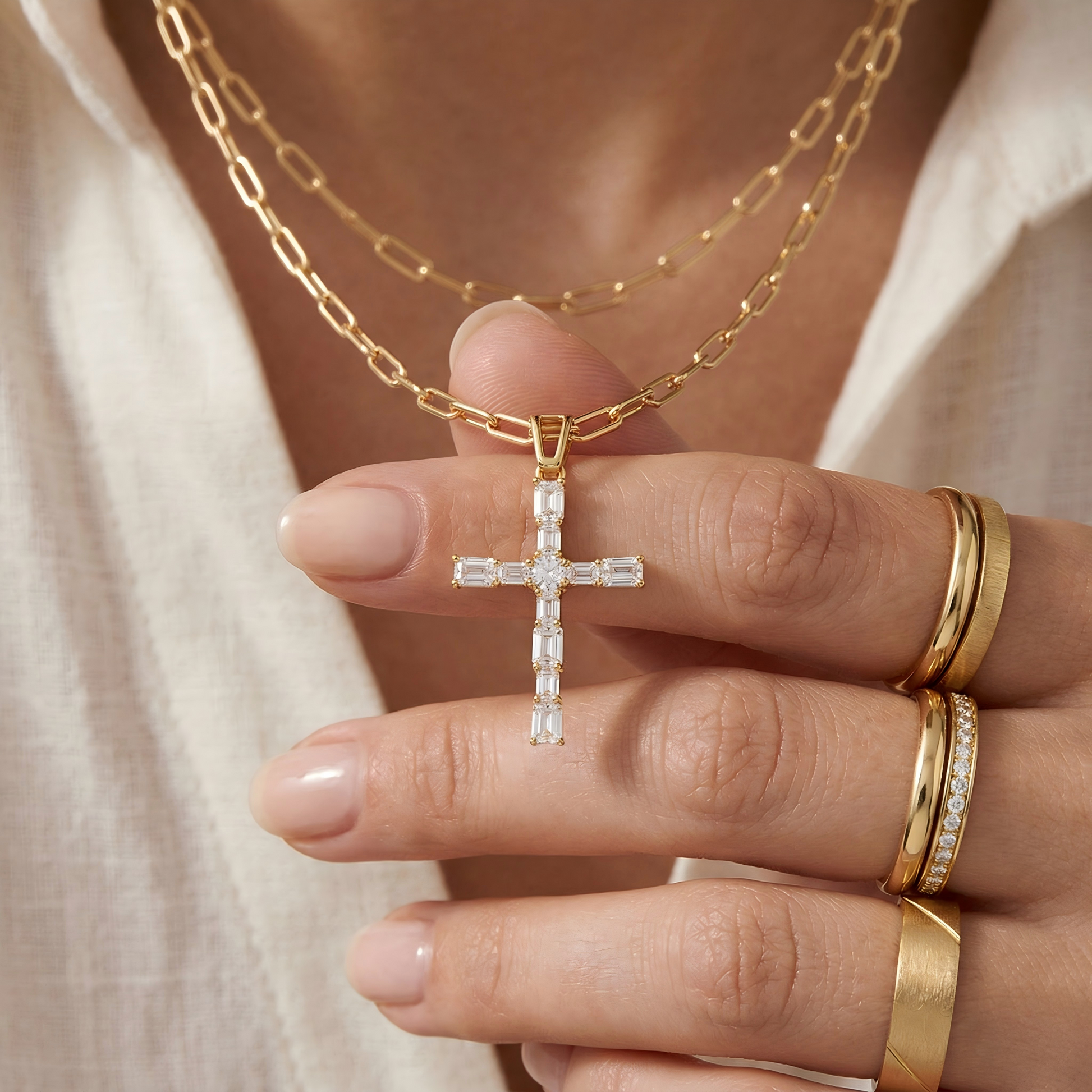 Close-up of a hand gently holding the necklace, fingers wearing matching rings, soft blurred white fabric background, natural skin texture, showing scale and intimate jewelry interaction.