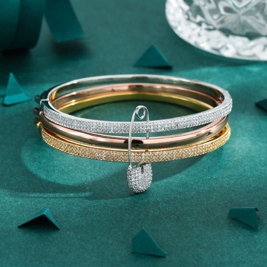 Stack of gold, rose gold, and silver bangles on a teal surface with a decorative glass object in the background.