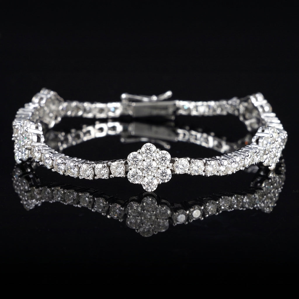 A silver-toned tennis bracelet with a central flower-shaped cluster of clear stones, displayed on a glossy black reflective surface.