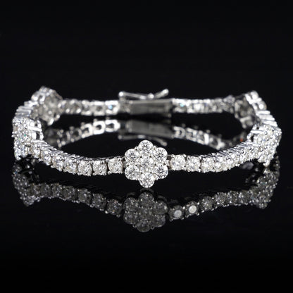 A silver-toned tennis bracelet with a central flower-shaped cluster of clear stones, displayed on a glossy black reflective surface.
