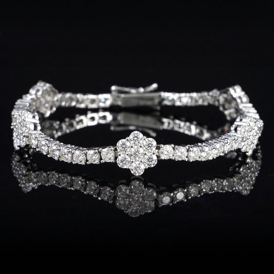 A silver-toned tennis bracelet with a central flower-shaped cluster of clear stones, displayed on a glossy black reflective surface.