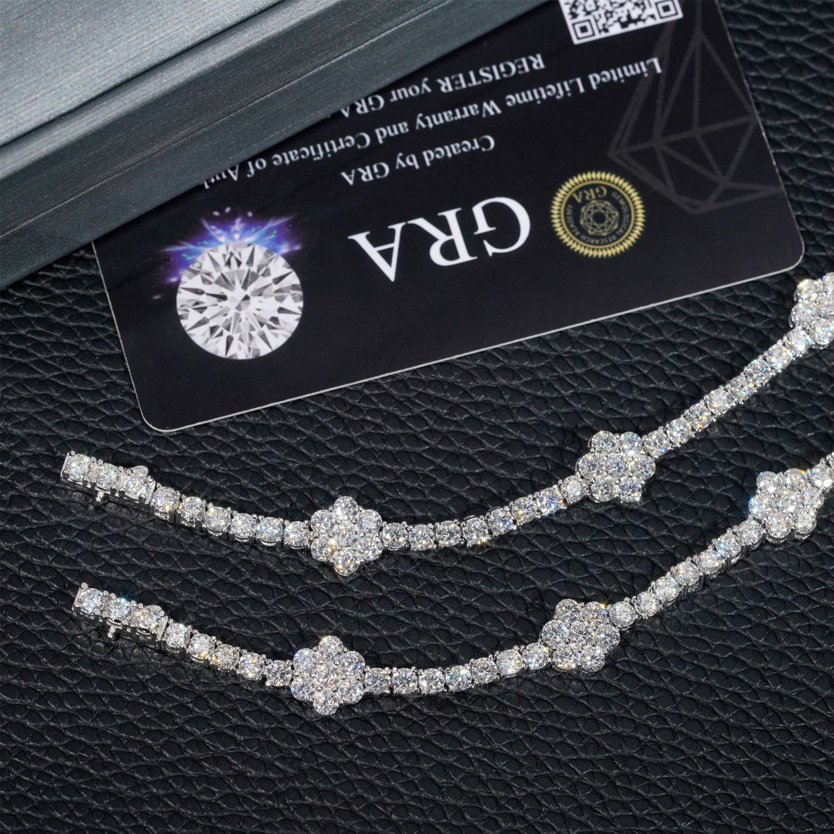 Two diamond-studded chain bracelets displayed on a textured black surface next to a black GRA certification card and a dark presentation box.