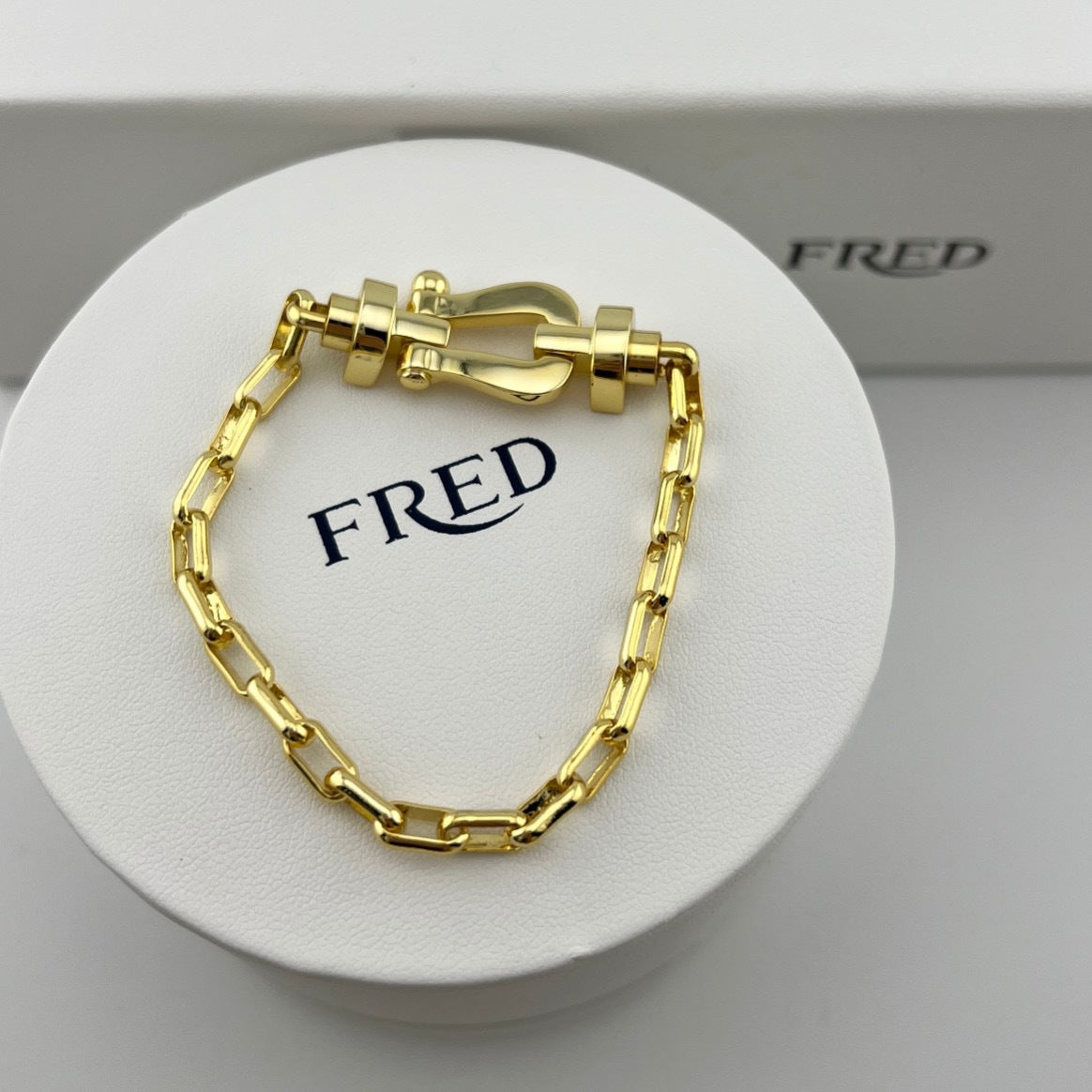Gold chain bracelet on a white stand with 'FRED' branding.