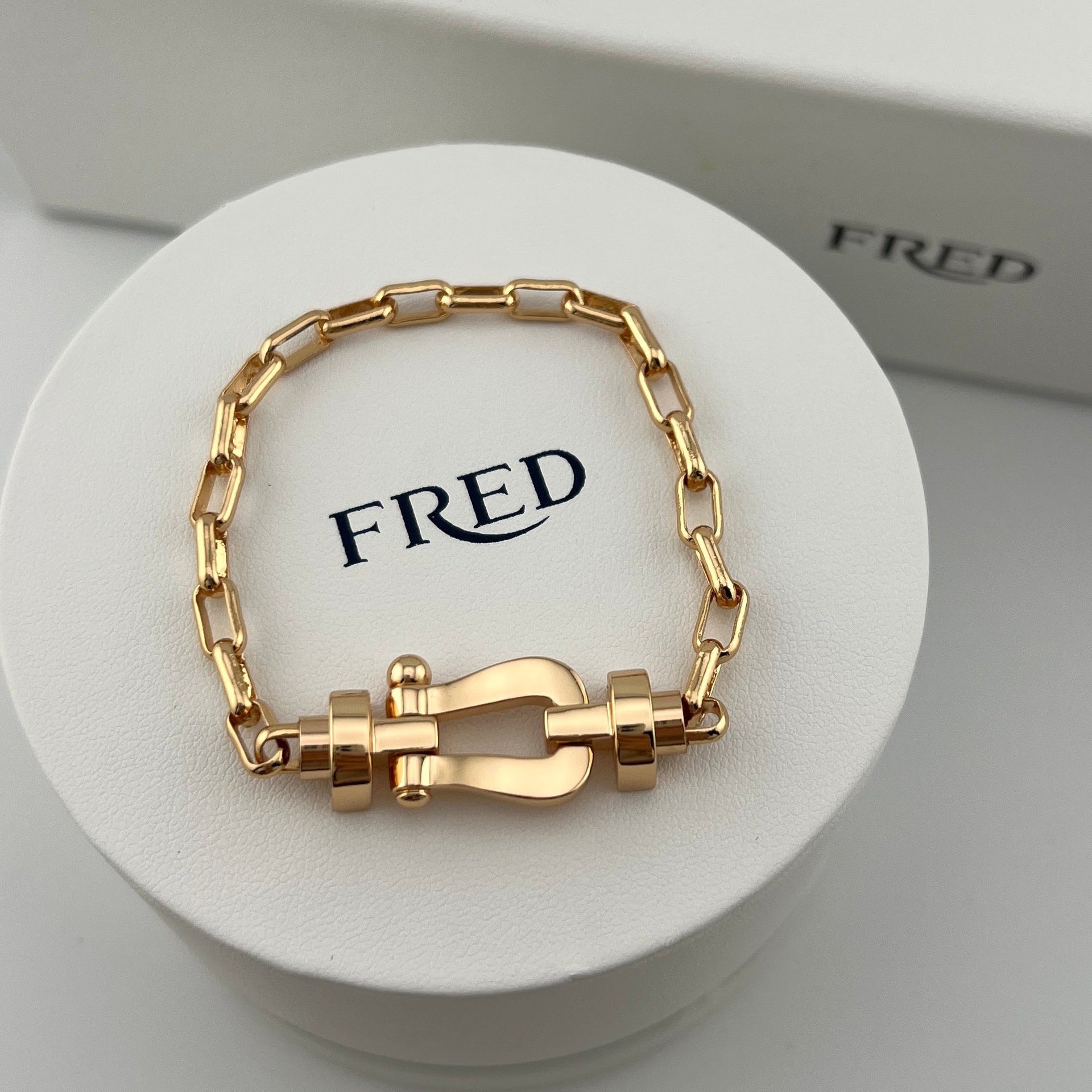 Gold chain bracelet on a white stand with 'FRED' branding.